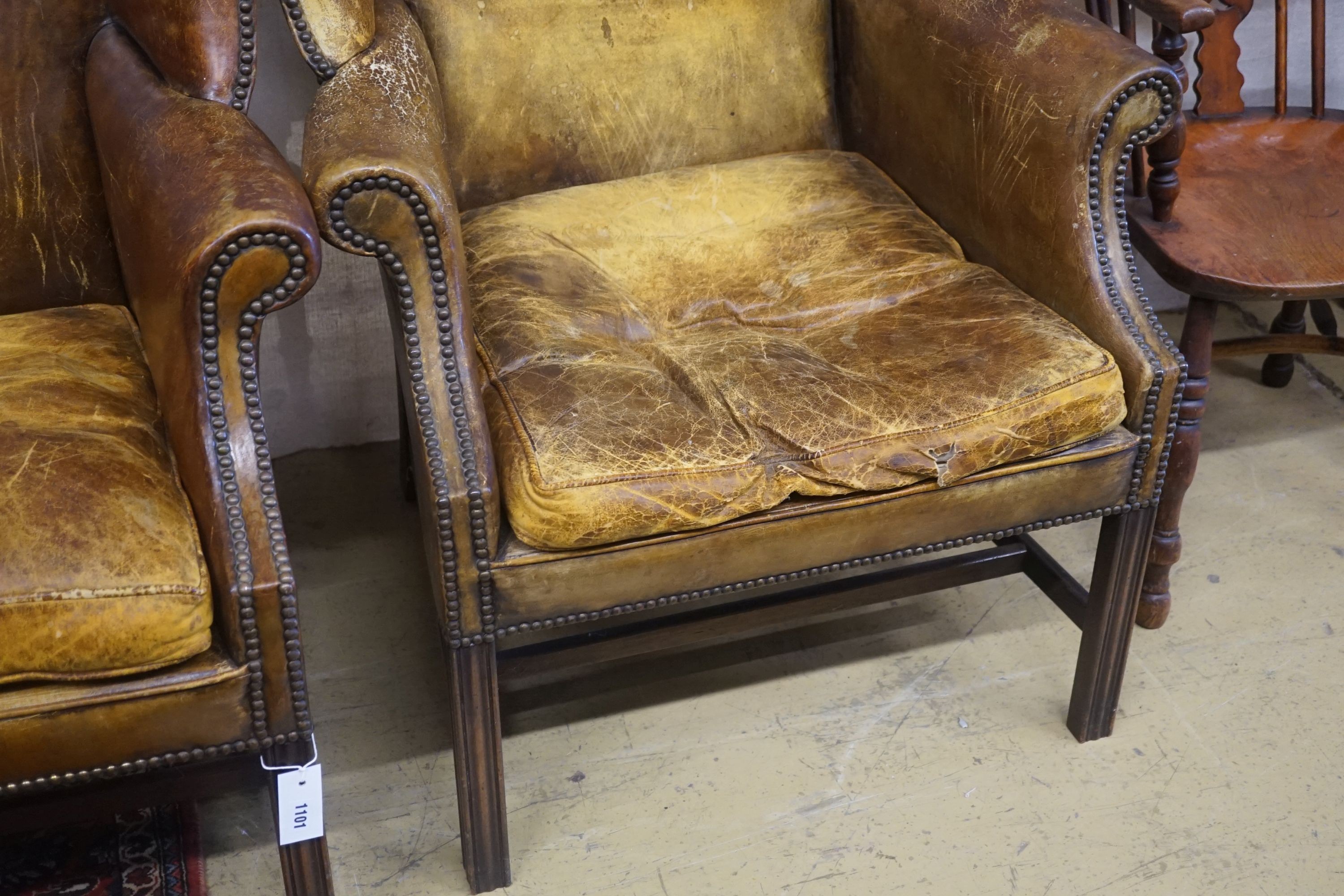 A pair of George III style tanned leather wing armchairs